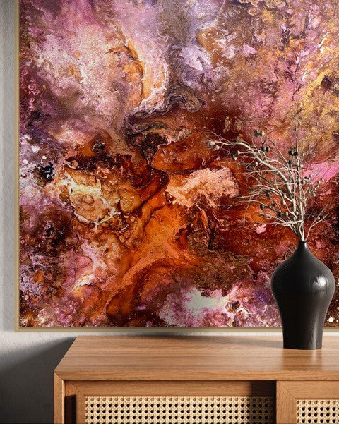 Abstract art piece with pink and orange hues on a wall above a wooden console table.