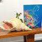 Large shell on a wooden surface with a colorful painting in the background
