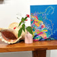 Colorful coral reef painting on a blue background with a large shell and pink vase on a wooden surface.
