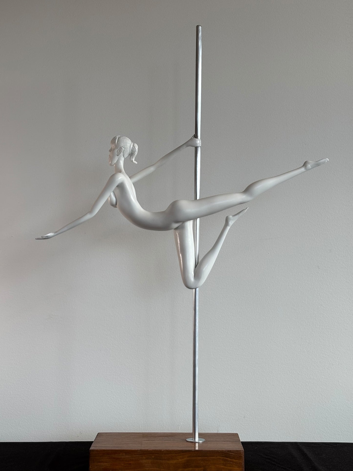 Silver pole dancing sculpture on a wooden base against a plain wall