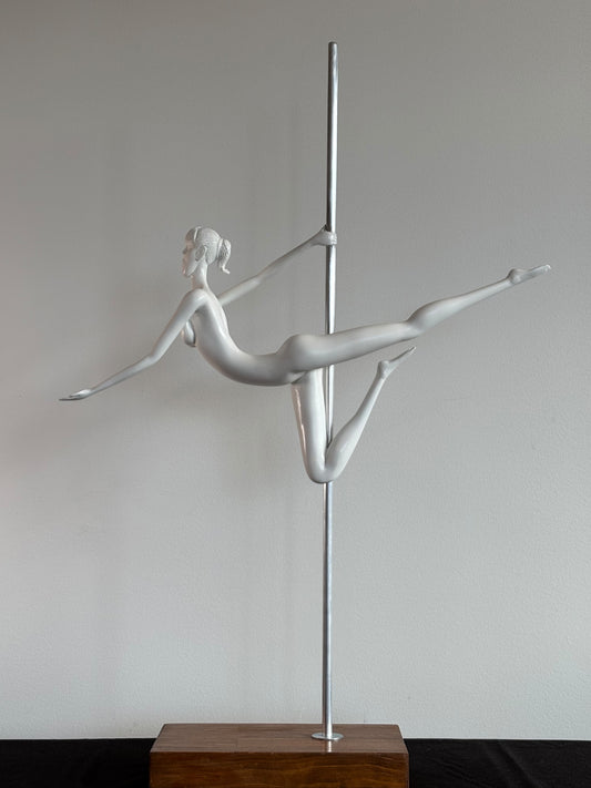 Silver pole dancing sculpture on a wooden base against a plain wall