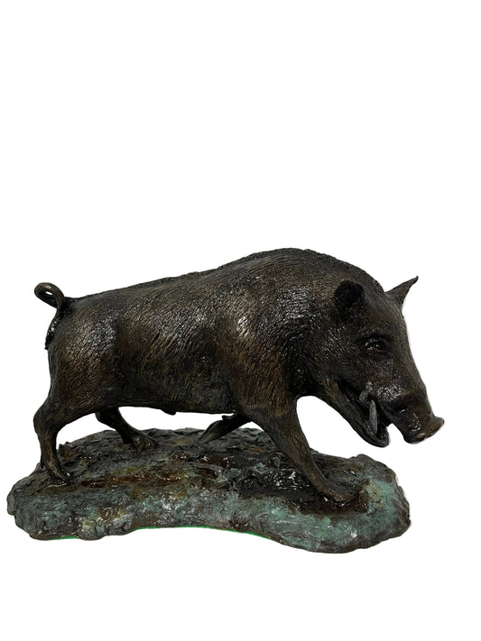 A dark bronze pig sculpture standing on a textured, mossy base, photographed against a plain white wall and display platform.