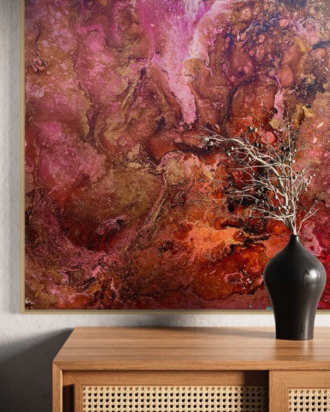 Abstract art piece with pink and brown colors on a wall above a wooden console table with a black vase.