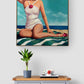 A framed art print depicting a retro-style woman in a white swimsuit on a striped beach towel, displayed on a light gray wall above a wooden dresser with a potted plant and a small book.